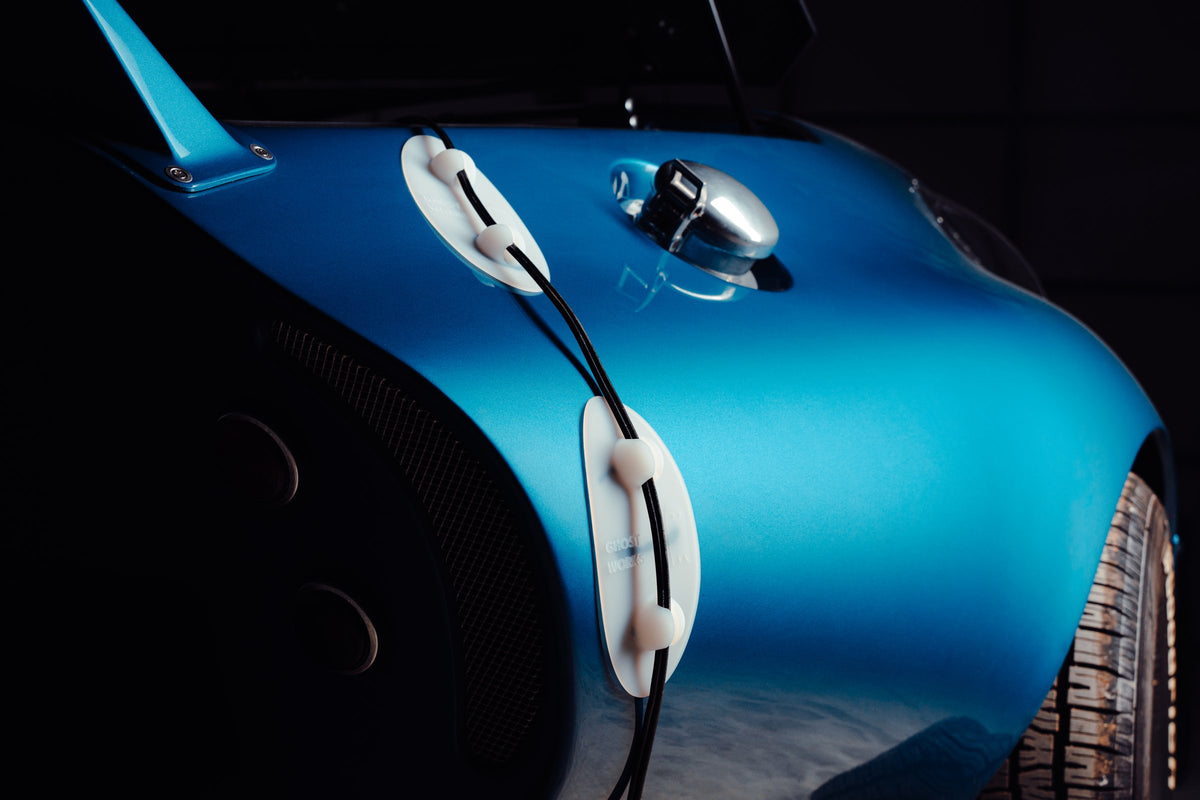 Two Ghost Guards routing a charging cable over a blue car's fender